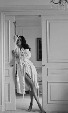 a woman in a bathrobe leaning on the door to reach into her room