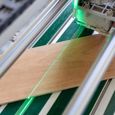 a piece of wood being cut by a machine with green laser light on it's side