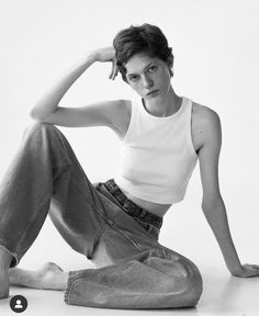 a woman sitting on the ground wearing jeans and a tank top with her hands behind her head