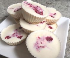 four cupcakes with white frosting and raspberry topping on a plate