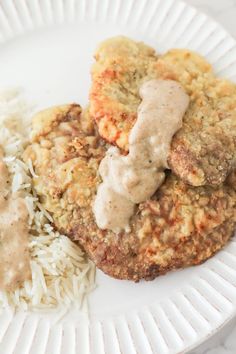 a white plate topped with meat patties covered in gravy next to rice