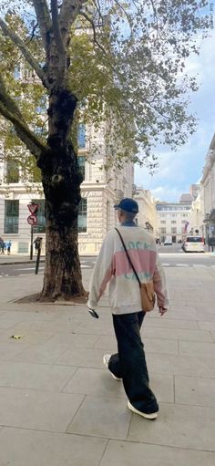 a man is walking down the sidewalk in front of a tree