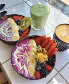 two bowls filled with different types of fruit on top of a table next to a drink