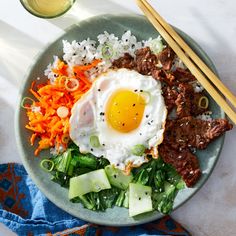 a plate with meat, rice and an egg on it next to chopsticks