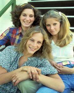 three women sitting next to each other on the steps in front of stairs with their arms around one another