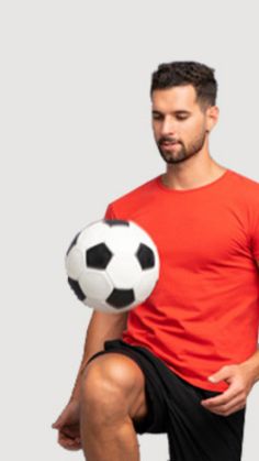 a man holding a soccer ball in his right hand and sitting on the ground while looking at it