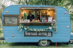 a man and woman are standing in the back of an old blue trailer that has been converted into a bar