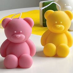 two plastic teddy bears sitting next to each other on a white table with yellow and pink decorations