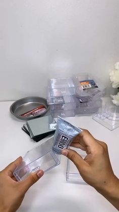 two hands are holding up some plastic containers on a white table with flowers in the background