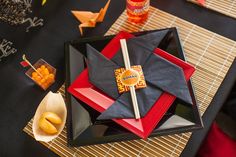 a black and red plate topped with an origami paper boat next to other plates