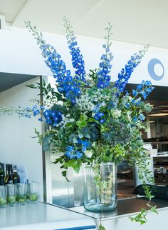 a vase filled with blue flowers sitting on top of a counter next to bottles and glasses