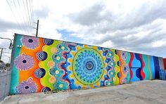 a large colorful mural on the side of a building with clouds in the sky behind it