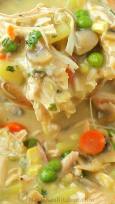 a spoonful of chicken noodle soup with carrots and peas on it is shown