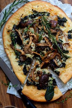 a pizza sitting on top of a wooden cutting board next to a knife and fork