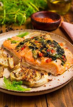 a white plate topped with salmon and artichokes on top of a wooden table