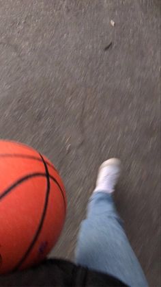 an orange basketball sitting on the ground next to someone's feet and leg in blue jeans