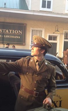 a man in uniform is standing next to a car and looking up at the sky