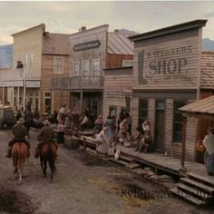 an old western town with people riding horses