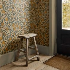 a wooden stool sitting in front of a wall with a floral design on it's side