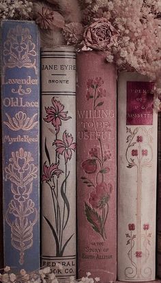 several books are lined up on a shelf with flowers in the middle and one is pink