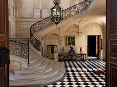 an ornate staircase with black and white checkered flooring, chandelier and painting on the wall