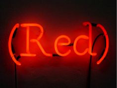 a red neon sign is lit up against a dark wall with the word red on it