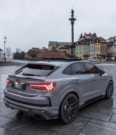 the rear end of a grey car parked in front of some buildings