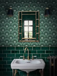 a white sink sitting under a mirror next to a green tiled wall with gold fixtures