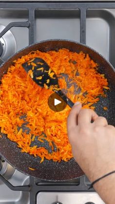 someone is frying shredded carrots in a skillet with a spatula on the side