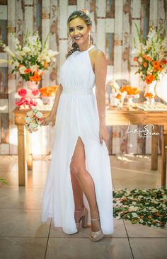 a woman in a white dress standing next to a wooden table with flowers on it