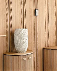 a white vase sitting on top of a wooden shelf next to a wall with wood paneling