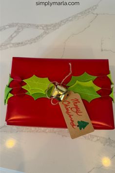 a red present wrapped in paper with holly leaves and bells on it, sitting on a table