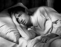 a black and white photo of a man laying in bed with his head on the pillow