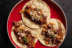 three tortillas on a red plate topped with meat and onions