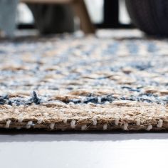 a close up of a rug on the floor with a chair in the back ground