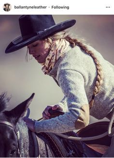 a woman riding on the back of a black horse wearing a cowboy hat and braids