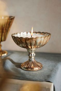 a candle that is sitting in a glass bowl on a table next to another one