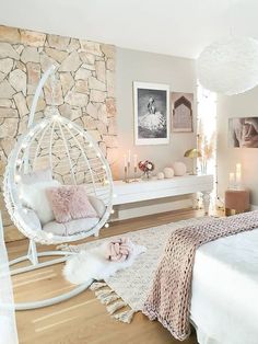 a bedroom with a white bed and hanging chair next to a stone wall in the corner