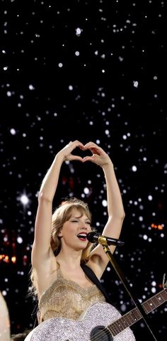 the singer is making a heart shape with her hands as she sings into a microphone