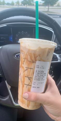 a person holding up a drink in front of a steering wheel with a green straw