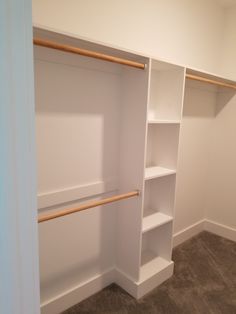 an empty closet with white shelves and wooden rails on the bottom shelf, next to carpeted flooring