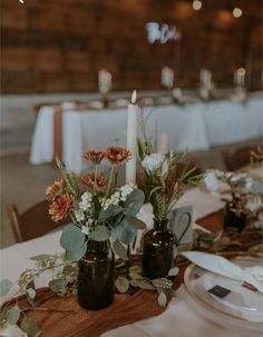 two vases filled with flowers sitting on top of a table next to plates and candles