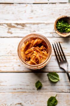 a glass jar filled with food next to a fork and bowl full of spinach