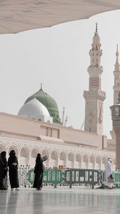 some people are standing in front of a large building with a green dome and white walls