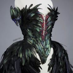 a mannequin with feathers and jewels on it's back, in front of a gray background