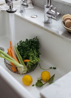 some vegetables are sitting in a basket on the kitchen sink next to two lemons