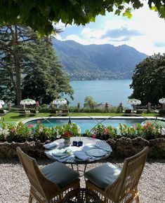 two wicker chairs sitting at an outdoor table next to a swimming pool with mountains in the background