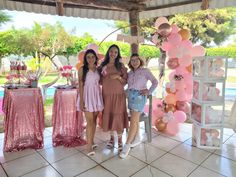 three women standing next to each other in front of a table with balloons on it