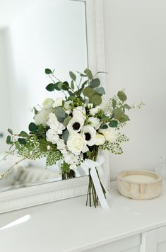 a bouquet of white flowers sitting on top of a table next to a mirror and bowl