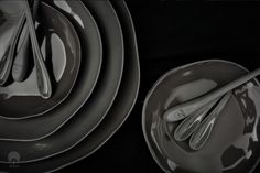 a stack of gray plates and spoons on top of each other in front of black background